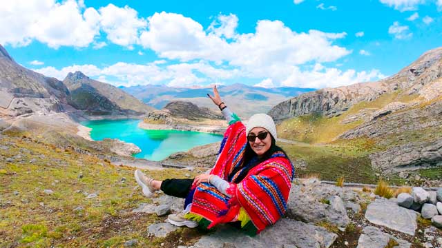 Turista con poncho frente a una laguna turquesa en Canta